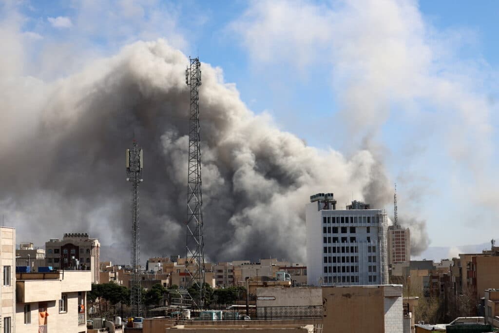 Nubes de humo oscuro se elevan sobre edificios en una ciudad, reflejando la tensión en Medio Oriente tras el anuncio del