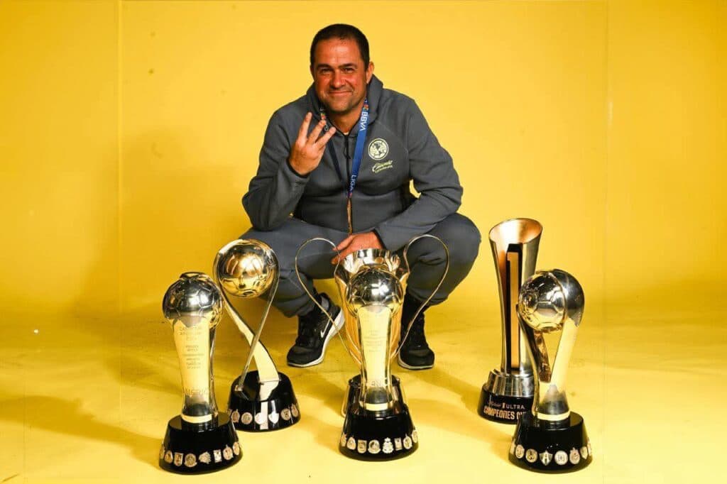 André Jardine posa junto a cuatro trofeos, mostrando el número tres con los dedos, simbolizando sus logros en el Club América.