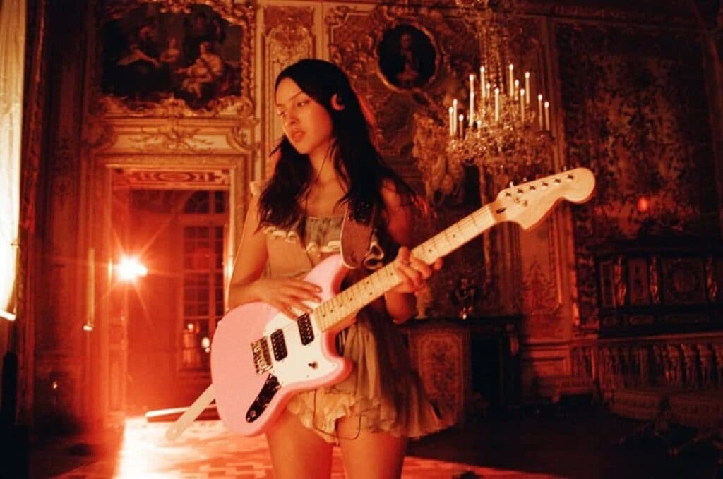 Mujer con guitarra rosa en un ambiente elegante y dorado, simbolizando el empoderamiento femenino en la música.