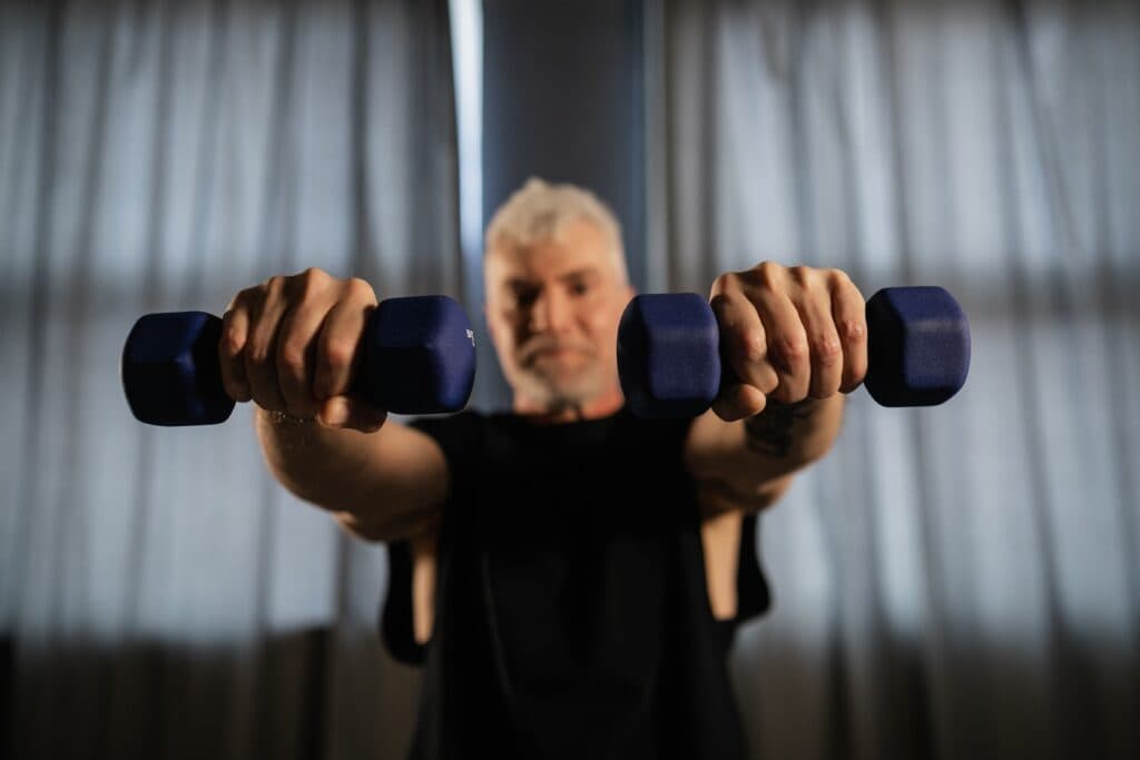 Hombre mayor sosteniendo pesas en un entorno de entrenamiento, promoviendo el ejercicio de fuerza para mejorar la calidad de vida.