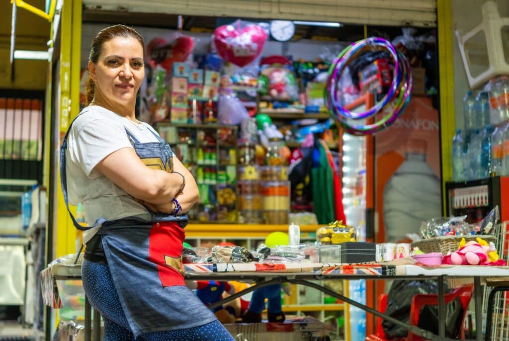 Mujer emprendedora en su tienda de Tijuana, rodeada de productos y artículos para la venta, simbolizando el impulso a nuevos negocios.