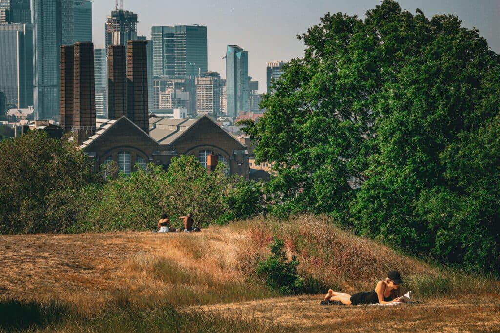 Personas descansando en un área verde de Londres, con edificios modernos de fondo, reflejando el calor extremo en el Reino Unido.