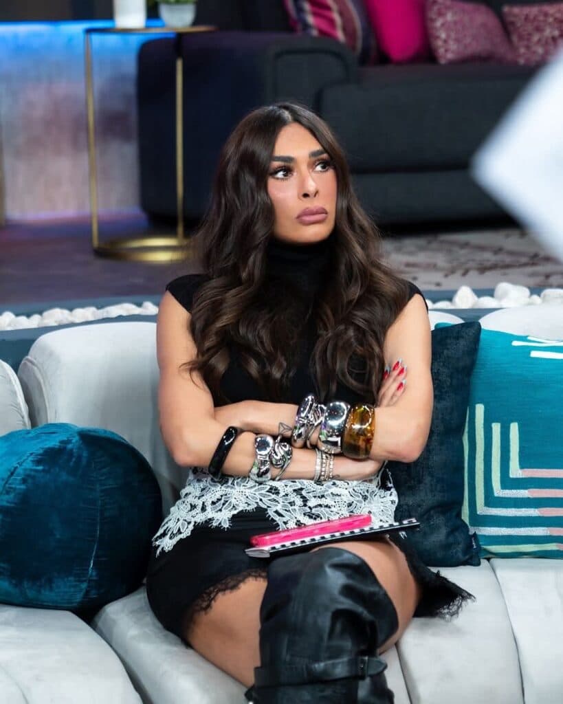 Galilea Montijo sentada en un sofá, con una expresión seria, luciendo un atuendo negro y accesorios brillantes, en el set de
