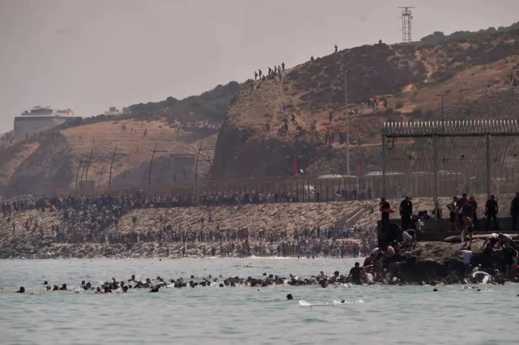 Migrantes intentando cruzar la frontera entre Marruecos y Ceuta, con un gran número de personas en la playa y en el agua.