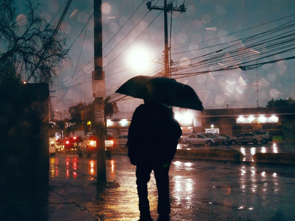 Persona con paraguas en una calle de la CDMX bajo lluvia intensa y tormenta eléctrica, reflejando condiciones climáticas adversas.