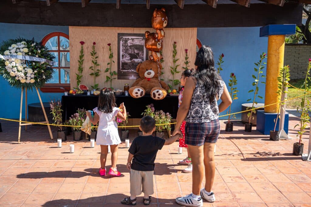 Niños y adultos rinden homenaje al Oso Yogi en un altar decorado con flores y globos en el Parque Morelos de Tijuana.